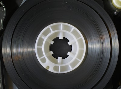 Close-up of tangled magnetic tape reels illuminated by eerie green light in a dark, cluttered lab.