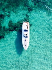 Aerial view of a luxury yacht sailing on clear blue water under a sunny sky.