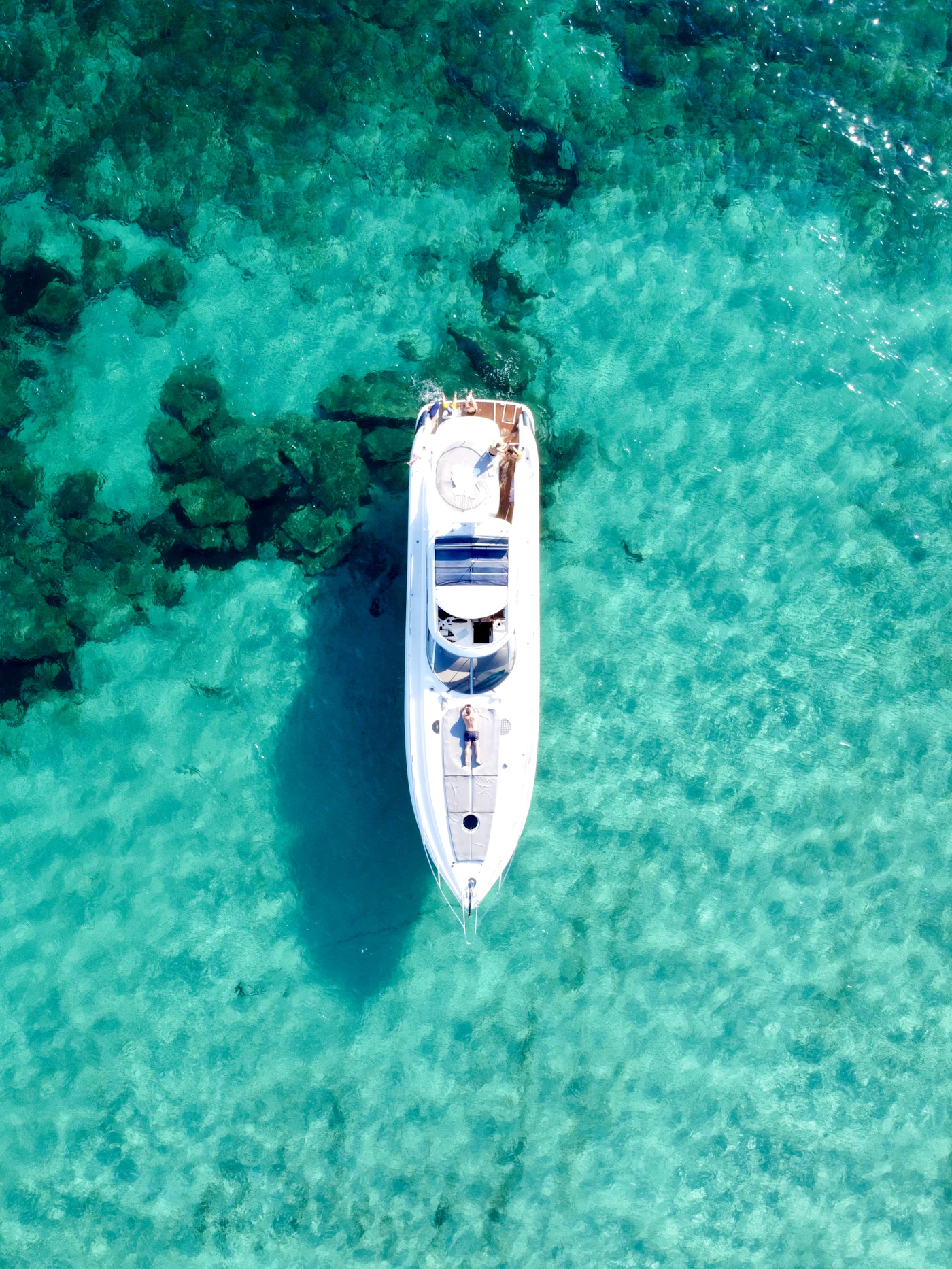 A yacht at anchor over turquoise water, seen from above
