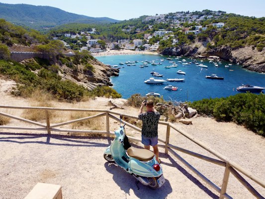 A person on a scooter looking at boats in the water — Ibiza, Spain