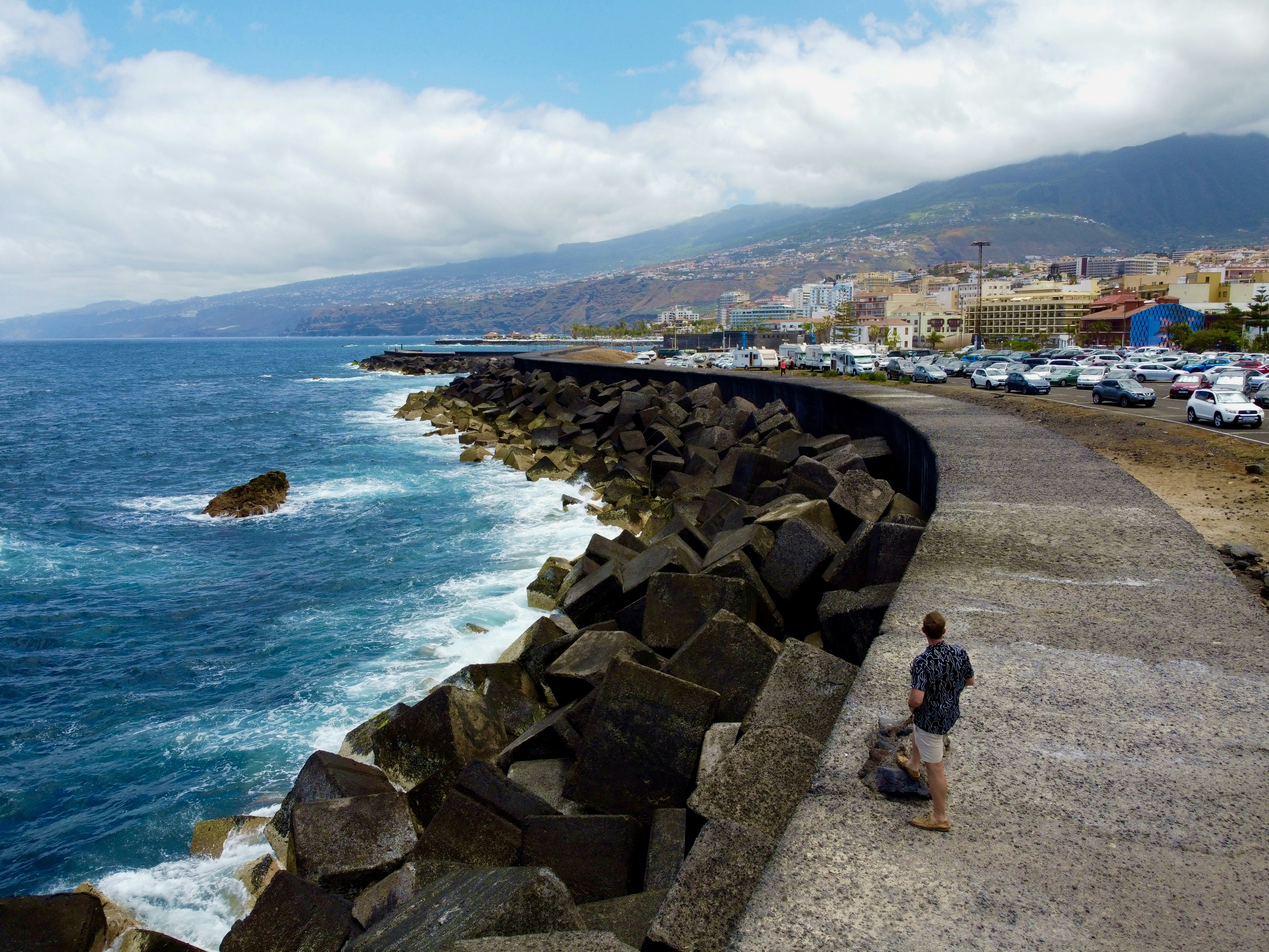a man sitting on the edge of a cliff next to the ocean, 