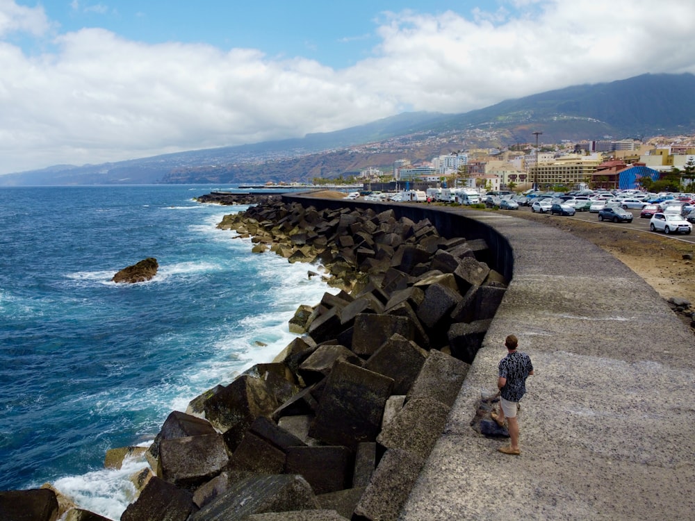 a man sitting on the edge of a cliff next to the ocean