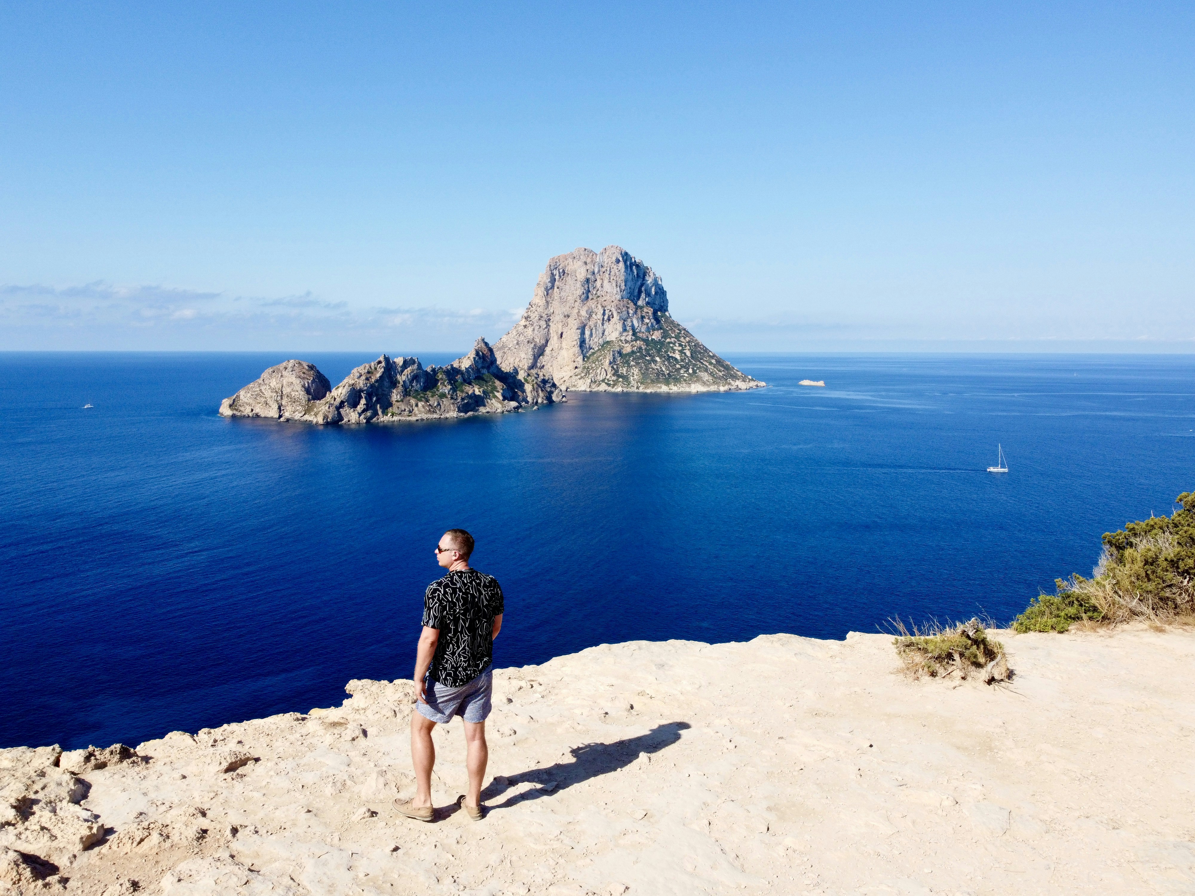 a man standing on a cliff overlooking the ocean, Drone shot in Ibiza, Spain.