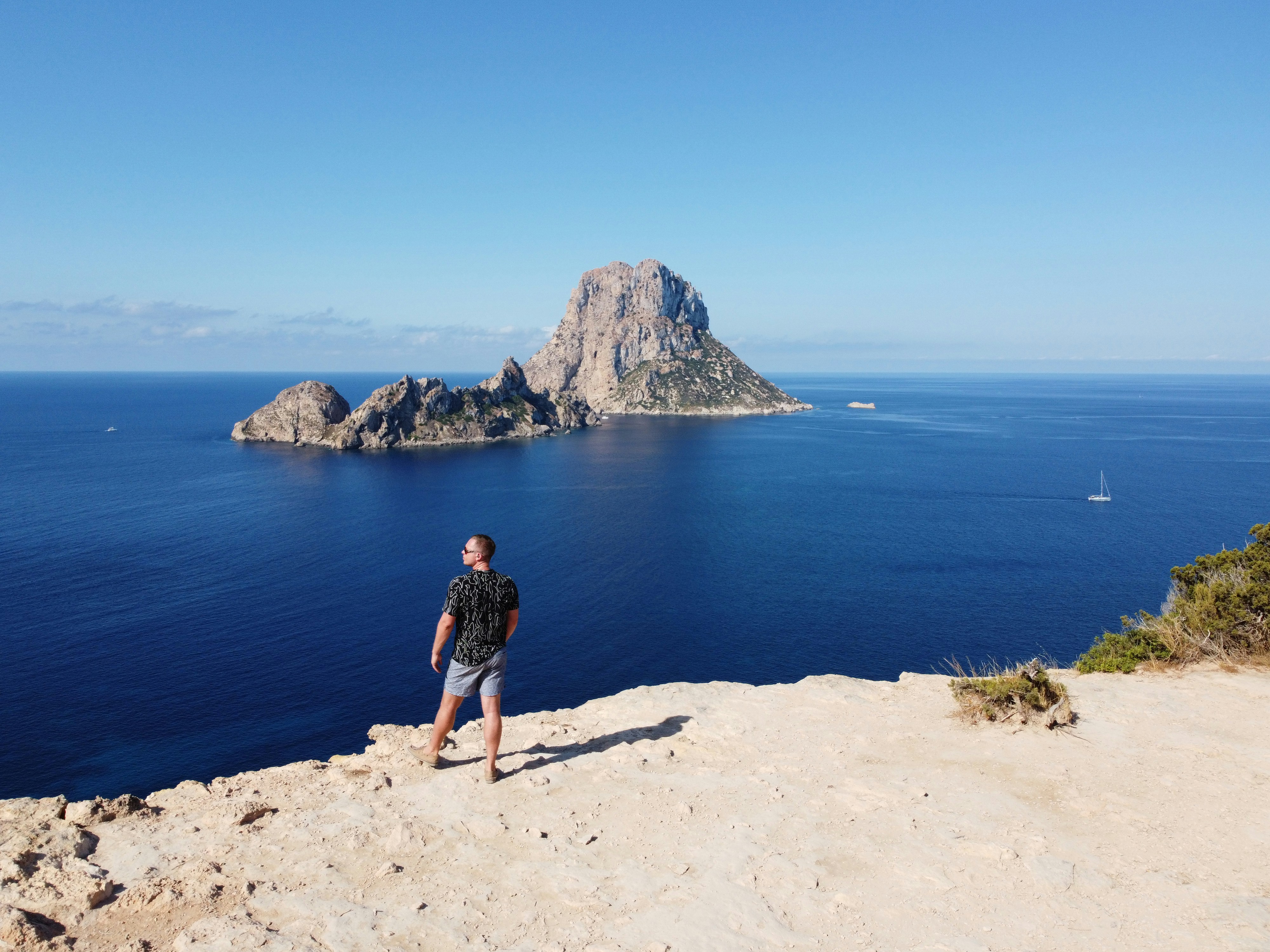 a man standing on top of a cliff next to the ocean, Drone shot in Ibiza, Spain.