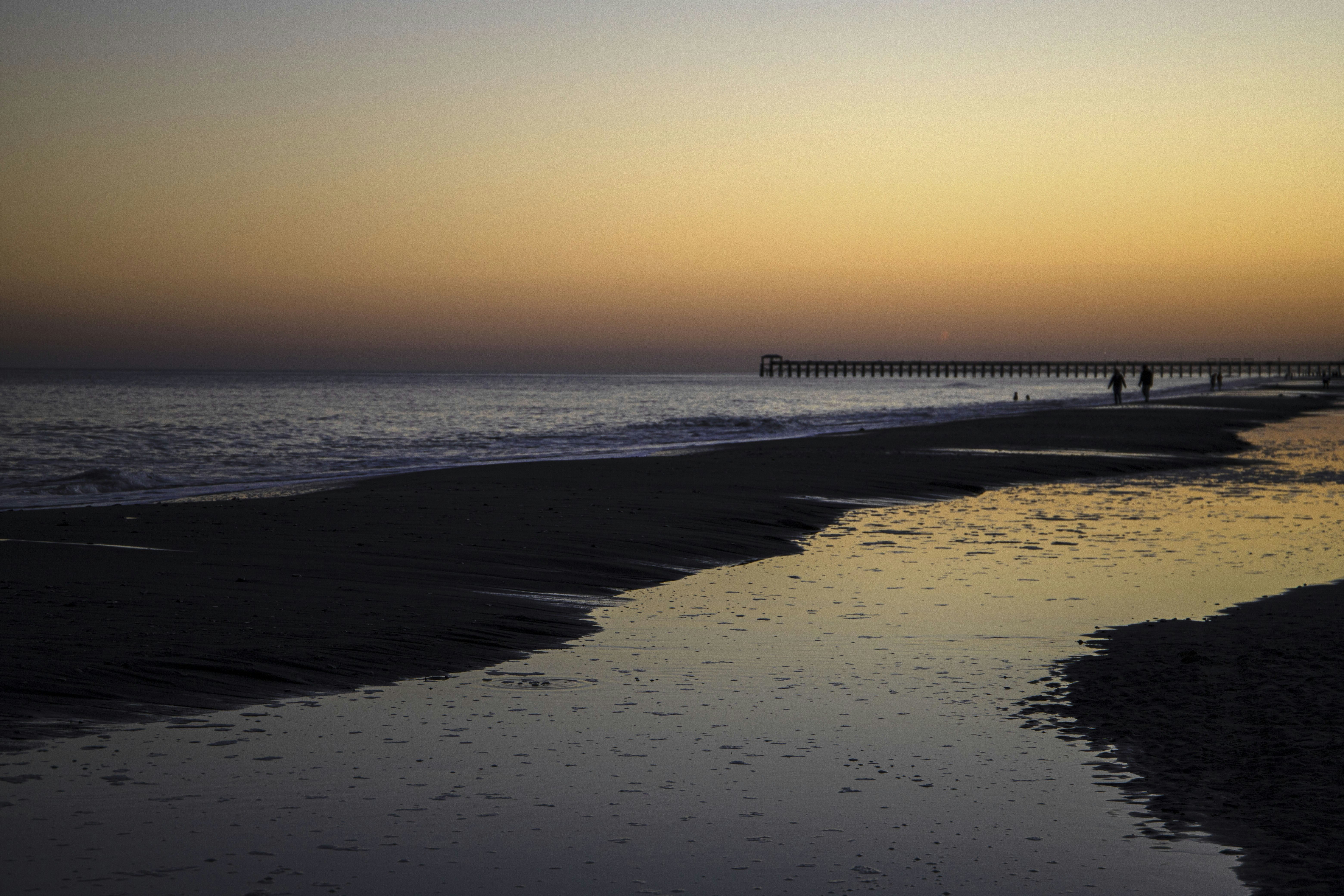 a couple of people standing on top of a beach next to the ocean, 