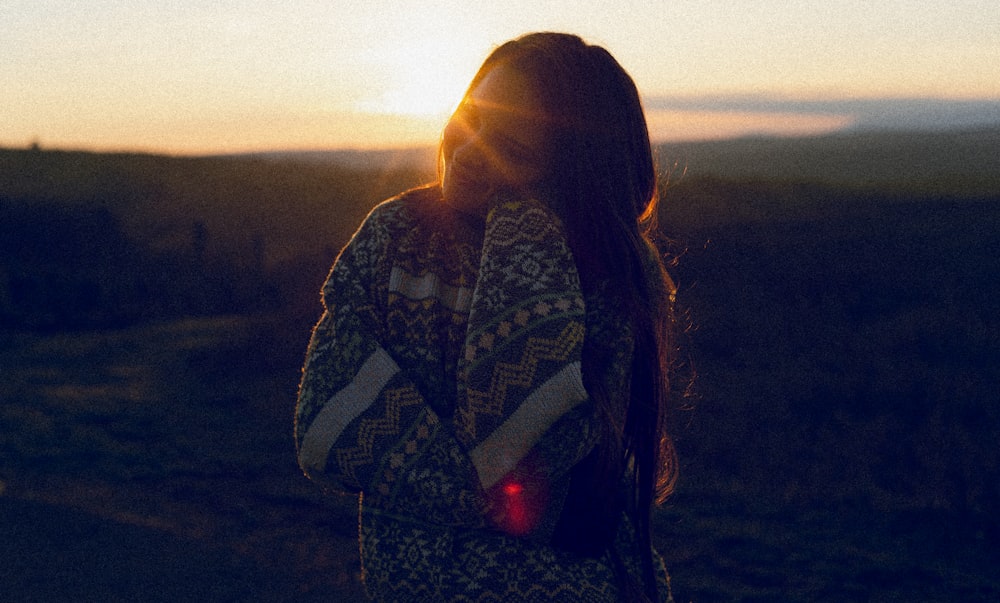 a woman standing in a field at sunset