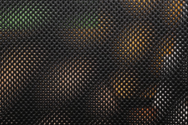 A close-up view of a mesh fabric. The pattern consists of small, evenly spaced holes creating a net-like effect. Through the mesh, hints of green and orange colors are visible, possibly indicating objects or surfaces behind it.