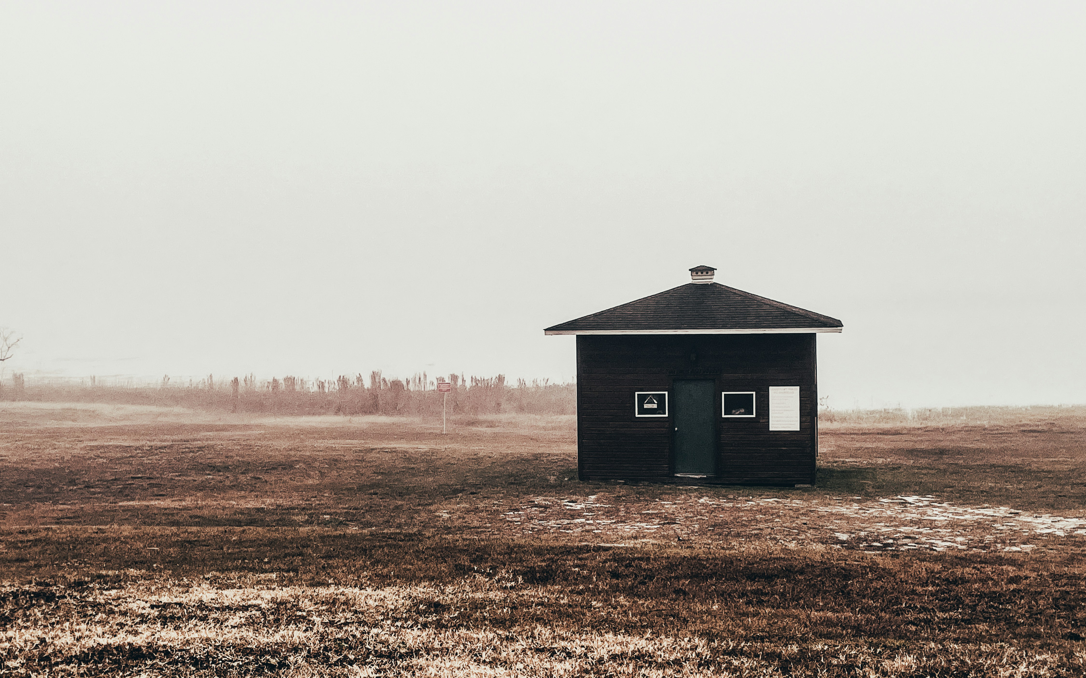 a small black building in a field on a foggy day