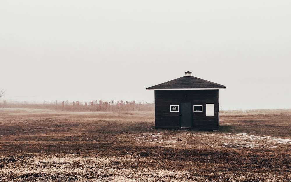 a small black building in a field on a foggy day