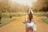 a woman walking down a dirt road carrying a purse