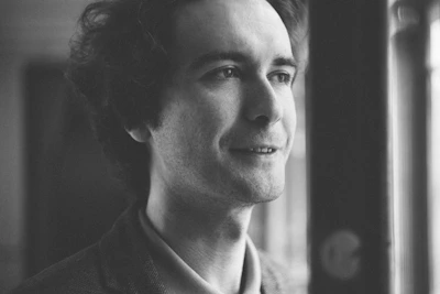 A black and white portrait of a thoughtful person looking out a window.