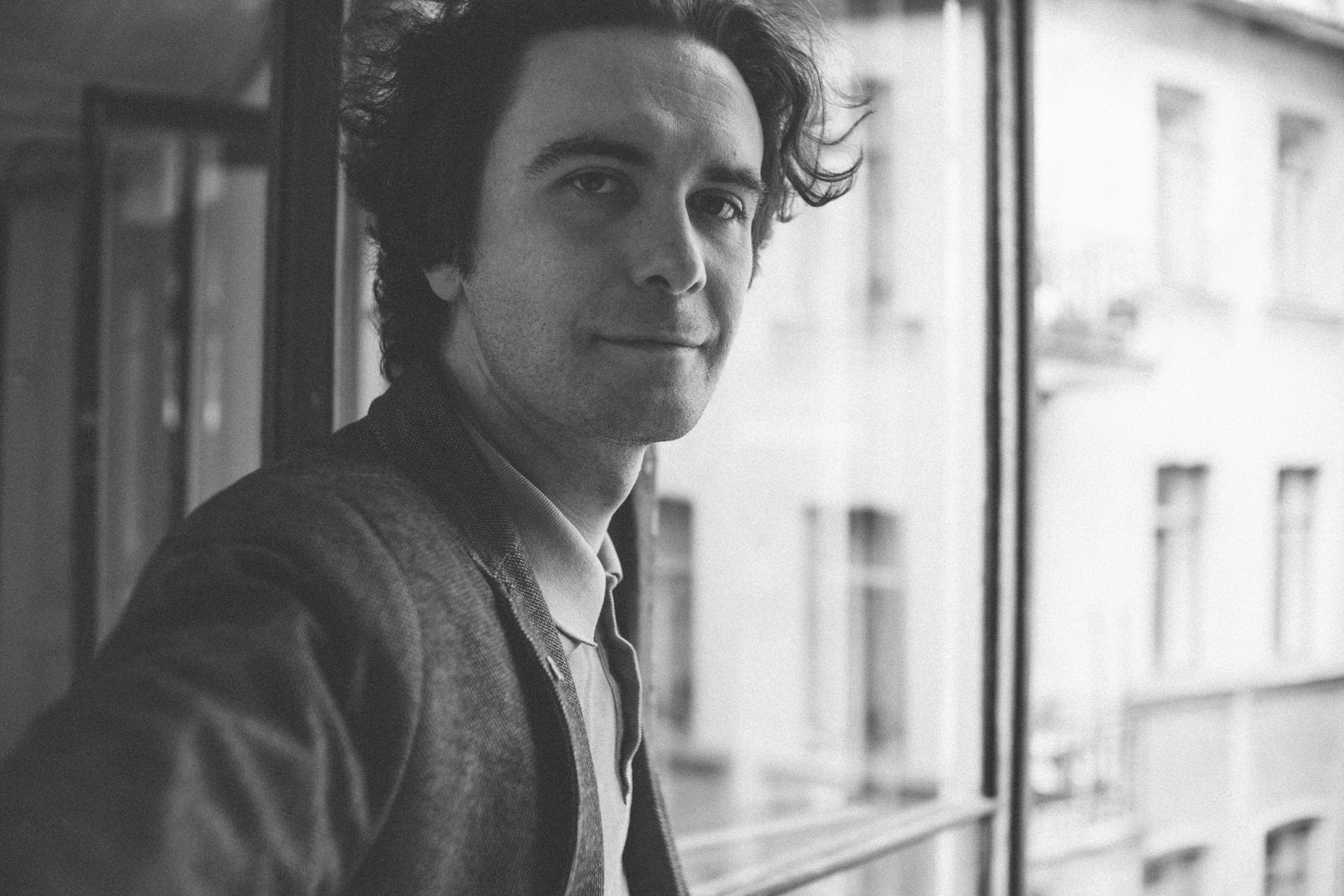 a black and white photo of a man looking out a window