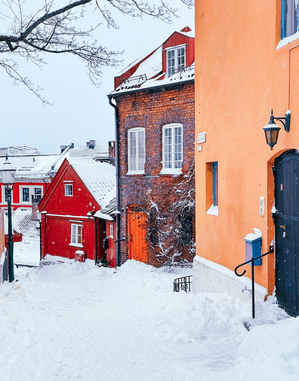 a snowy street with a red building and a tree
