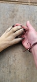 A human hand gently holding the paw of a dog, both resting on a textured concrete surface. The human wears a simple leather bracelet.