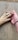 A human hand gently holding the paw of a dog, both resting on a textured concrete surface. The human wears a simple leather bracelet.