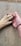 A human hand gently holding the paw of a dog, both resting on a textured concrete surface. The human wears a simple leather bracelet.