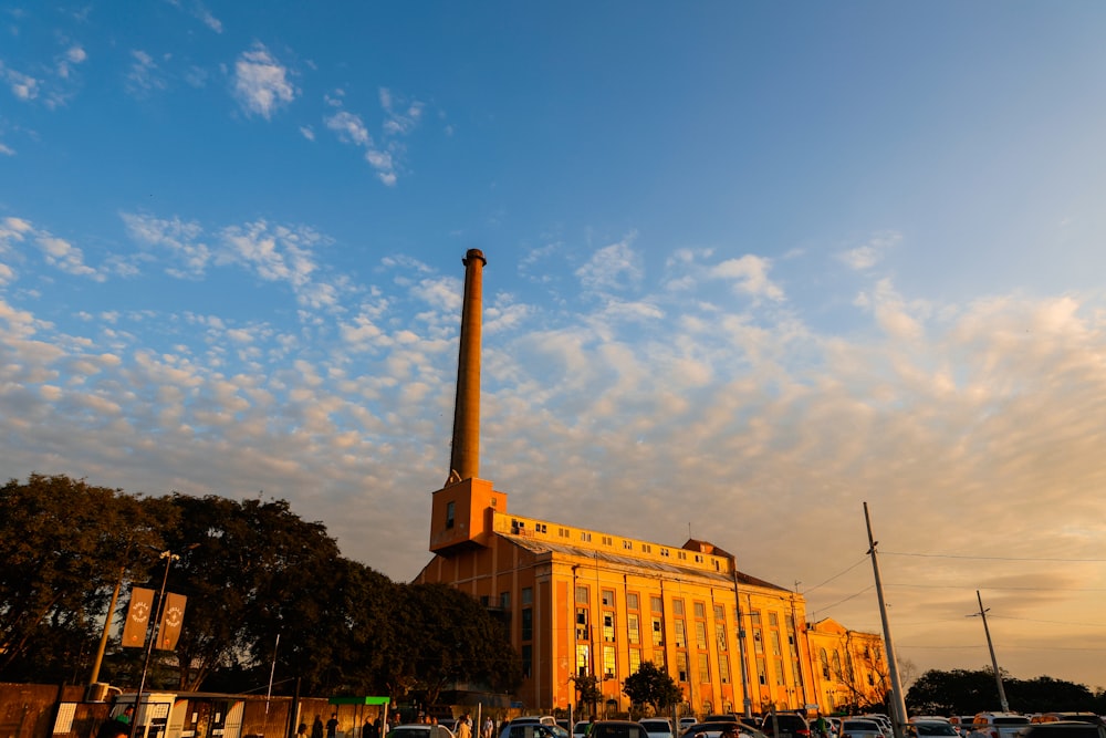 a factory building with a tall chimney in the middle of a parking lot