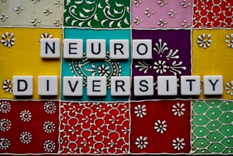 Scrabble tiles spell out 'neuro diversity' against a vibrant, ornate background composed of colorful square tiles with floral and geometric patterns.