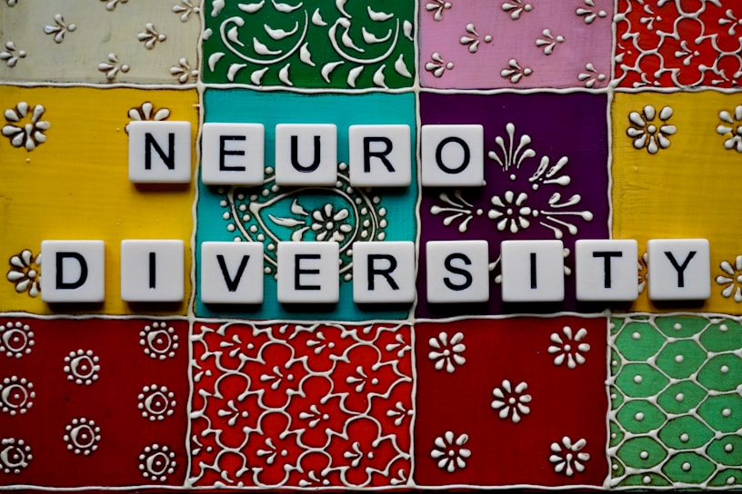 Scrabble tiles spell out 'neuro diversity' against a vibrant, ornate background composed of colorful square tiles with floral and geometric patterns.