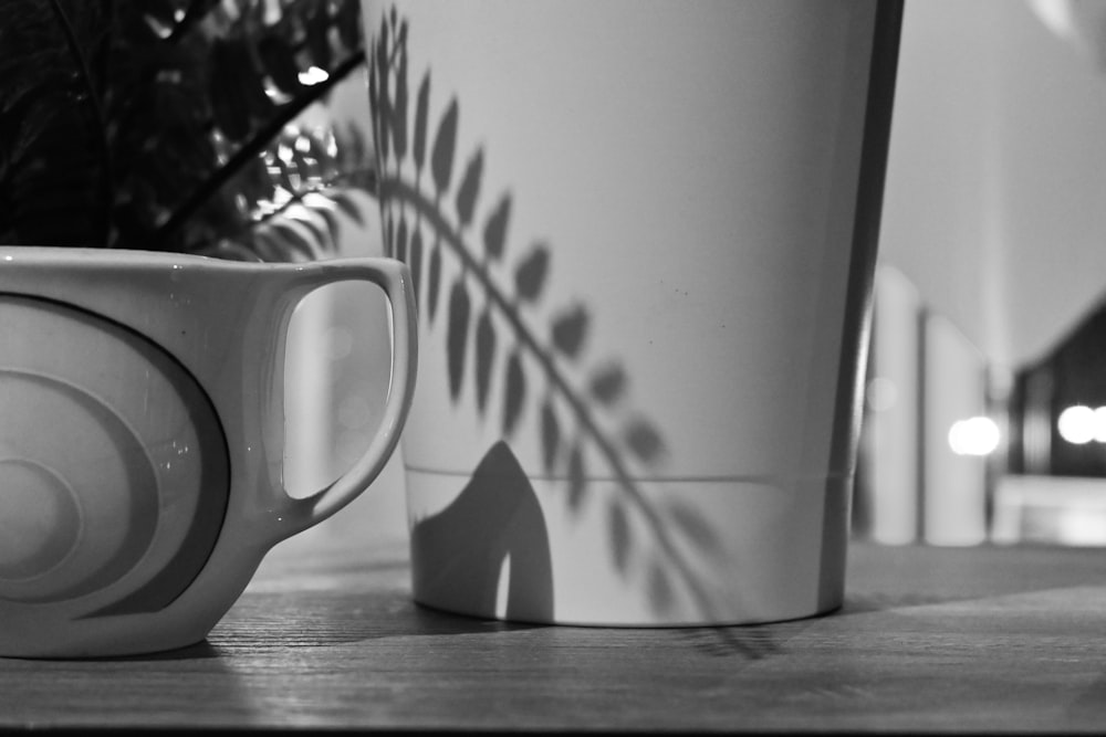 two coffee cups sitting on a table next to a potted plant