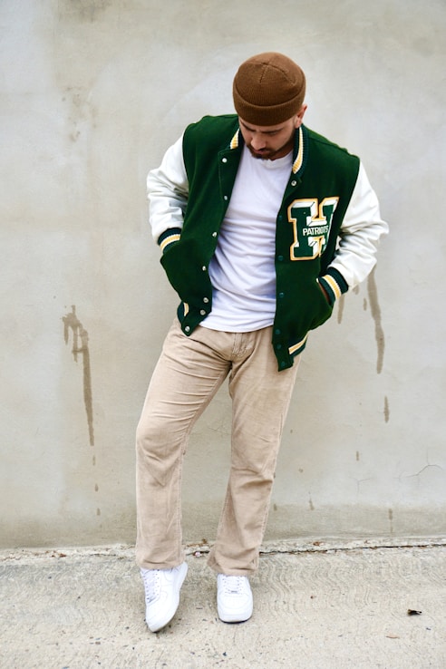 a man leaning against a wall wearing a green and white jacket