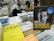 A cluttered bookstore counter with various books in Chinese and English, prominently featuring a book by Bear Grylls. Two individuals are seated in the background, engaged in reading or writing.