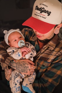 a man holding a baby wearing a red and white hat