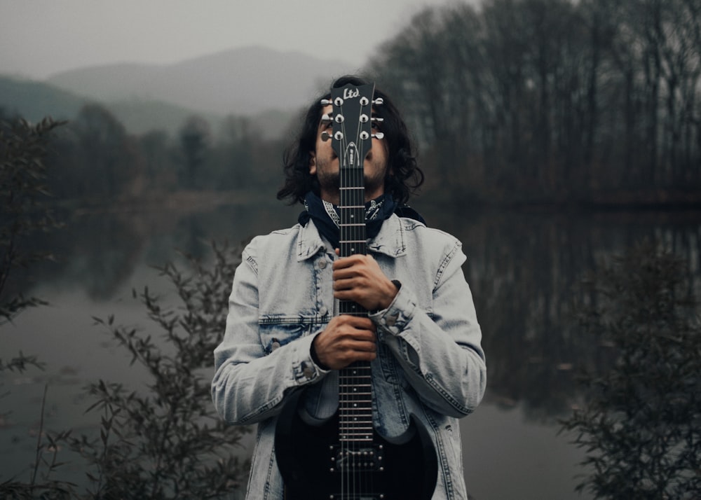 a man holding a guitar in front of a body of water