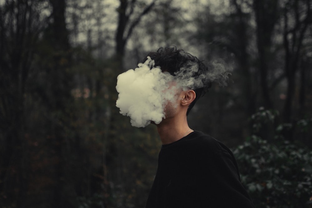 a man standing in a forest with a cloud of smoke coming out of his mouth