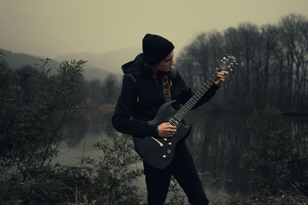 a man holding a guitar near a body of water