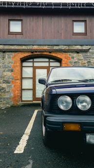 A vintage car parked beside a classic brick property, symbolizing the union of automotive and real estate heritage.