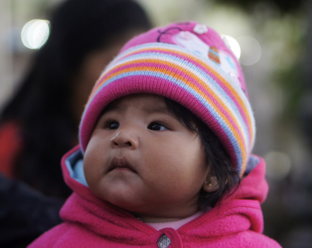 a small child wearing a pink coat and a colorful hat