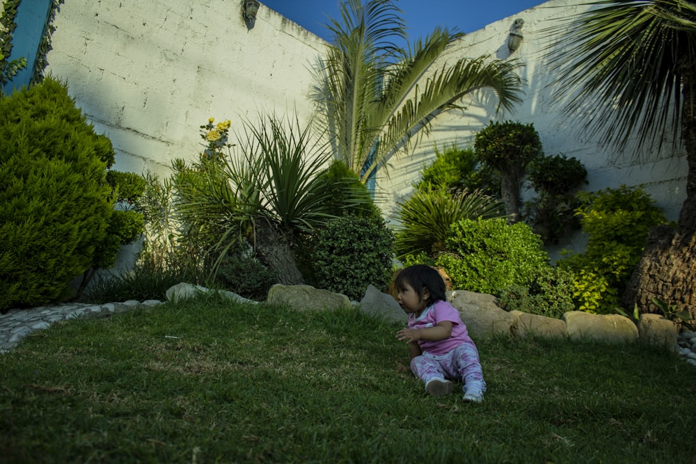 a little girl sitting in the grass next to a tree