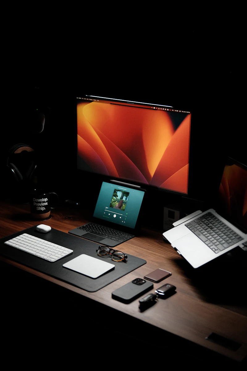 Laptop and monitor on a wooden desk in a dark workspace