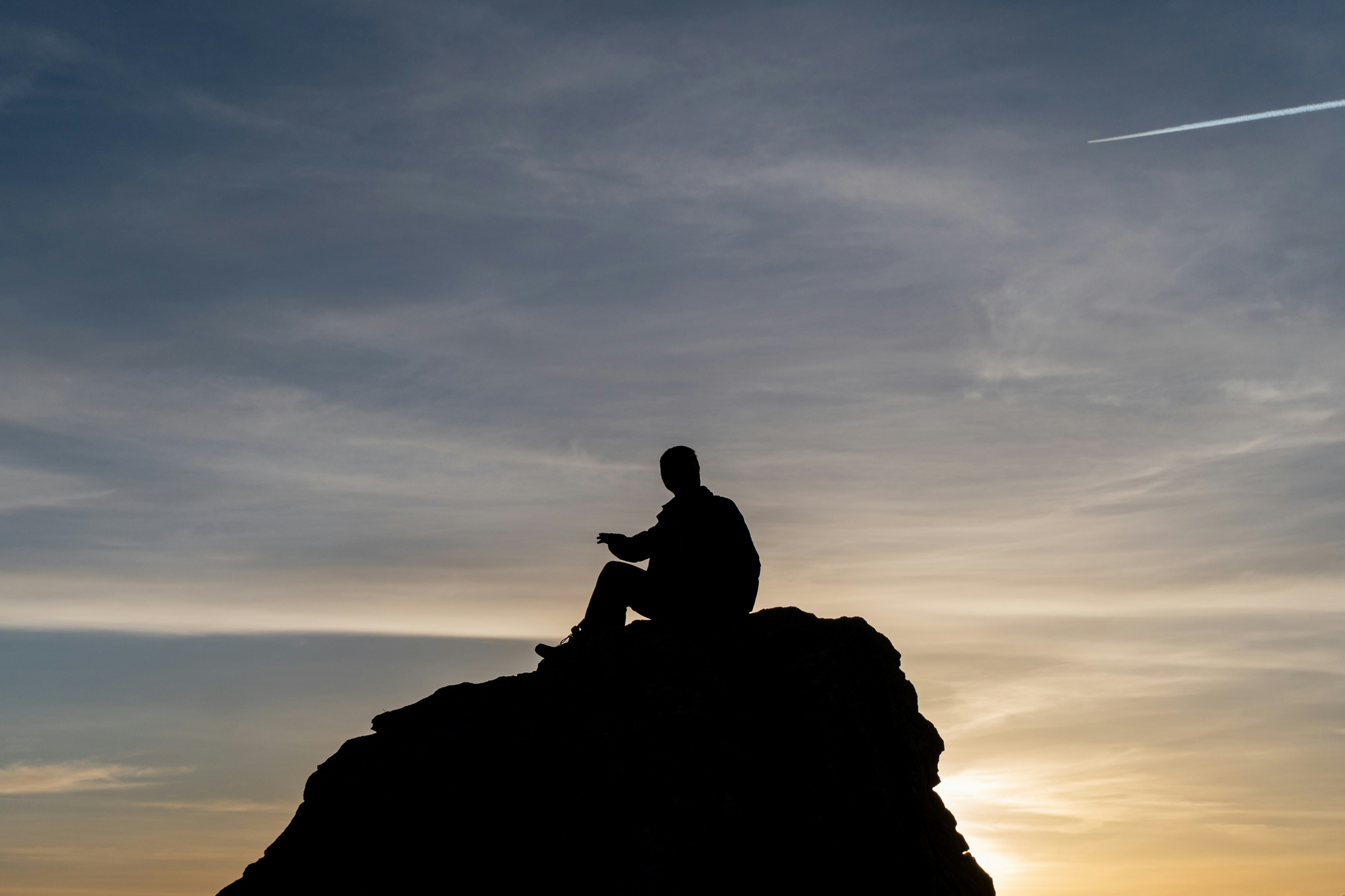 a man sitting on top of a rock while looking at his cell phone
