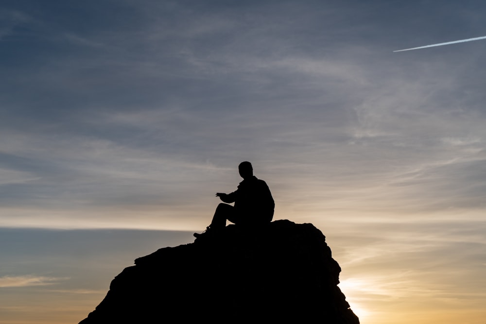 a man sitting on top of a rock while looking at his cell phone