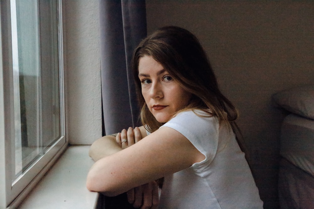 a woman leaning on a window sill looking out the window