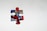 A single jigsaw puzzle piece with a colorful abstract design featuring red, blue, black, and white swirls, placed on a plain light gray background.