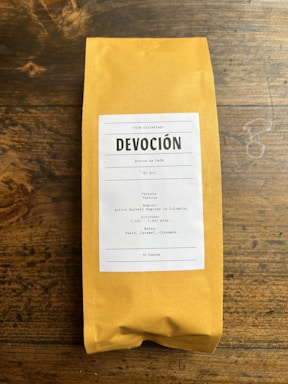 A package of coffee labeled 'DEVOCIÓN', featuring details about its Colombian origin, including variety, region, altitude, and flavor notes. The package is placed on a rustic wooden surface.
