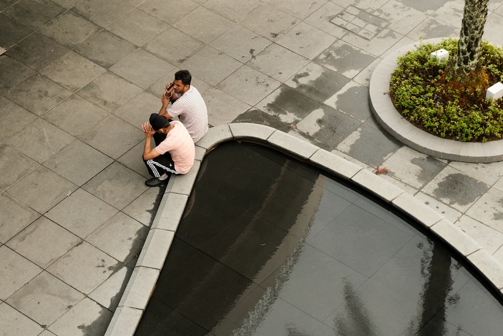 a couple of people sitting on the ground next to a pond