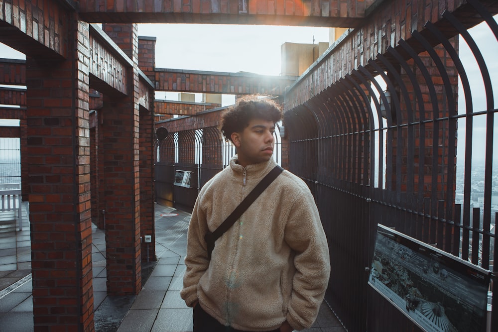 a young man standing on a sidewalk next to a fence