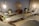 A serene and modern lounge area with several reclining chairs arranged around the room. The walls are adorned with a large circular decorative piece, and potted plants add a touch of greenery. Soft lighting from hanging lamps creates a warm ambiance. Small side tables hold plants and magazines, enhancing the inviting atmosphere.