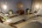 A serene and modern lounge area with several reclining chairs arranged around the room. The walls are adorned with a large circular decorative piece, and potted plants add a touch of greenery. Soft lighting from hanging lamps creates a warm ambiance. Small side tables hold plants and magazines, enhancing the inviting atmosphere.