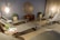 A serene and modern lounge area with several reclining chairs arranged around the room. The walls are adorned with a large circular decorative piece, and potted plants add a touch of greenery. Soft lighting from hanging lamps creates a warm ambiance. Small side tables hold plants and magazines, enhancing the inviting atmosphere.