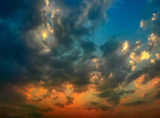 Dramatic clouds illuminated by vibrant colors create a striking sky. Deep blues are complemented by warm oranges and yellows, suggesting a sunset or sunrise scene.