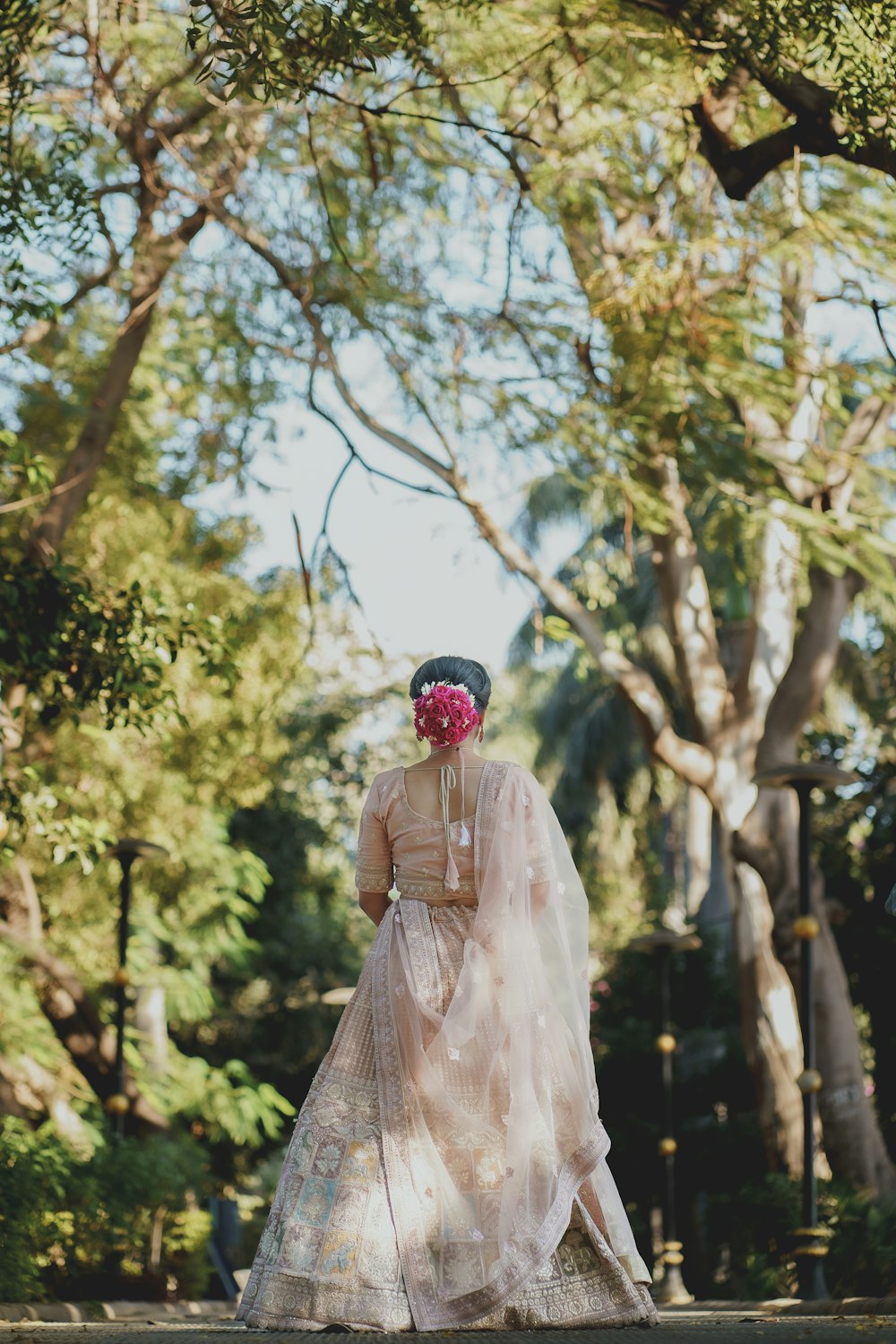 a woman in a dress and hat walking through a park