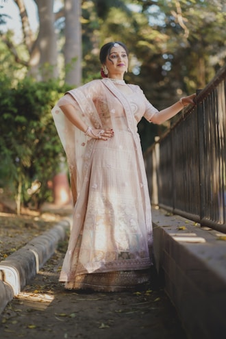 A graceful model wearing a pastel pink Pakistani suit with delicate threadwork standing in a sunlit courtyard.