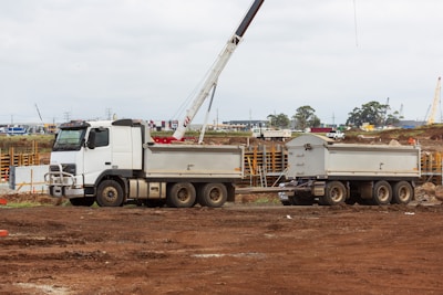 A bright orange delivery truck unloading construction materials at a busy site under a clear sky.