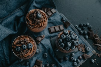 two glasses of chocolate pudding with blueberries on top