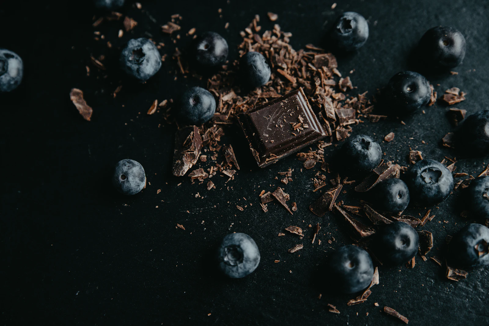 Quadrados de chocolate amargo ao lado de frutas vermelhas frescas sobre fundo escuro, iluminação cinematográfica